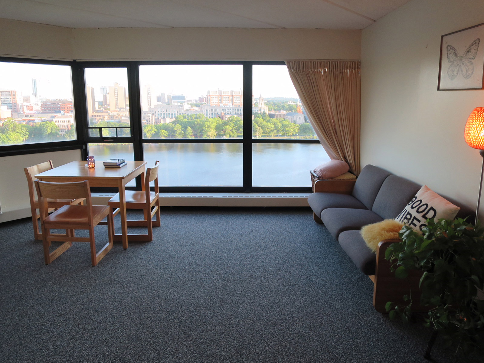 A living room with a sofa, dining table and large windows looking out towards the Charles River